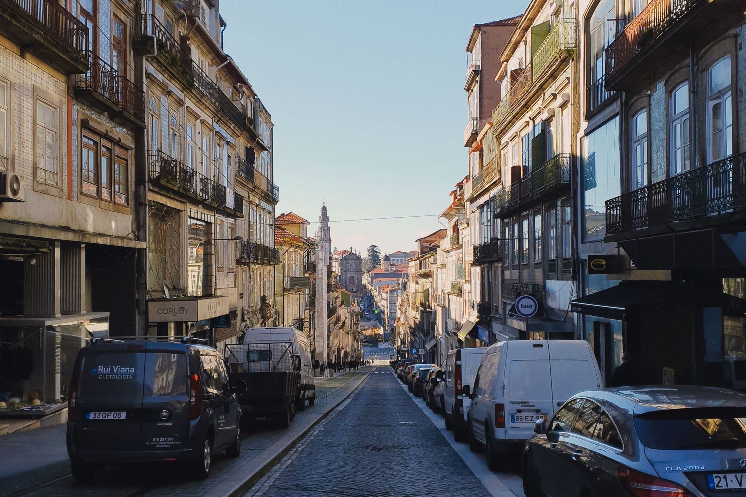 Rua empedrada do Porto com edifícios históricos e carros estacionados