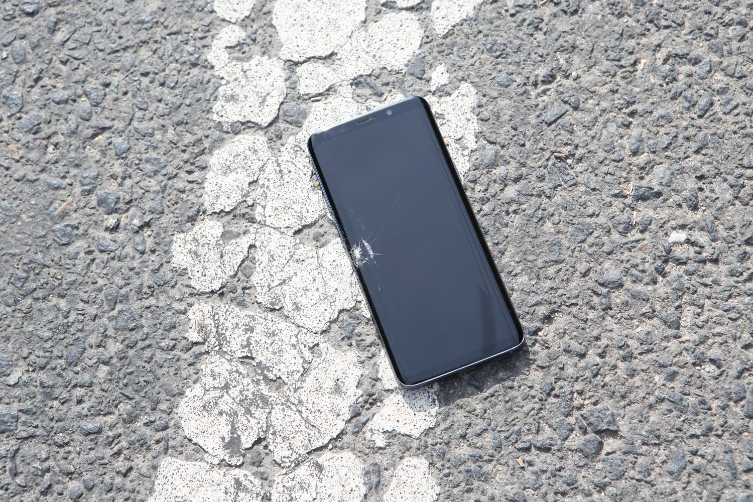 Telemóvel com o ecrã estalado caído no asfalto de uma rua