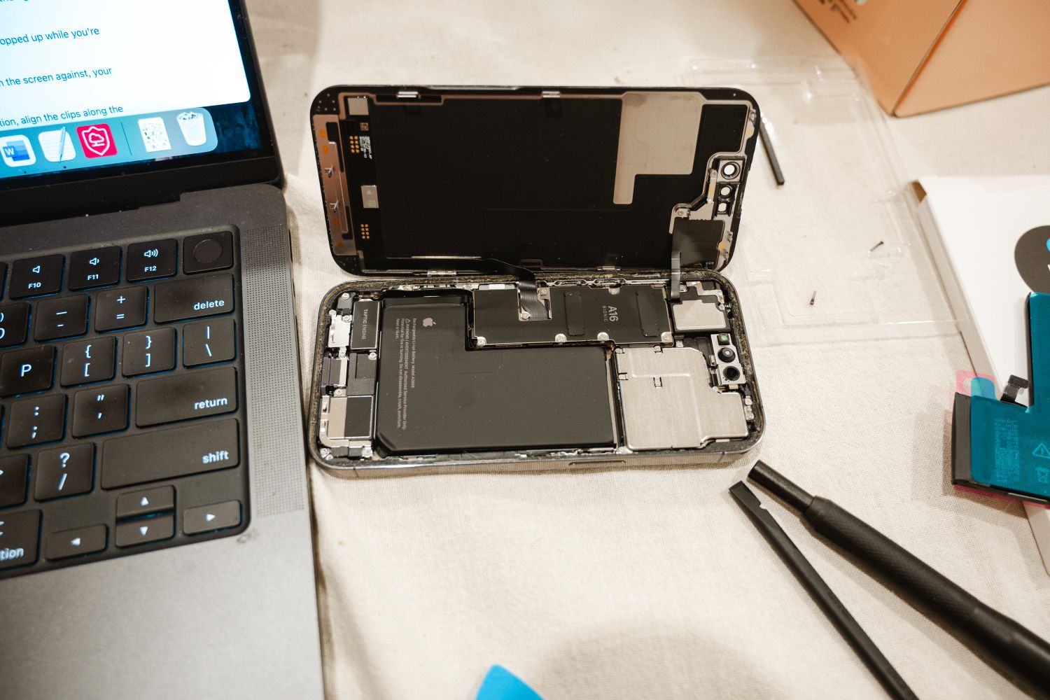 iPhone aberto durante uma substituição de bateria, com ferramentas de reparação ao lado