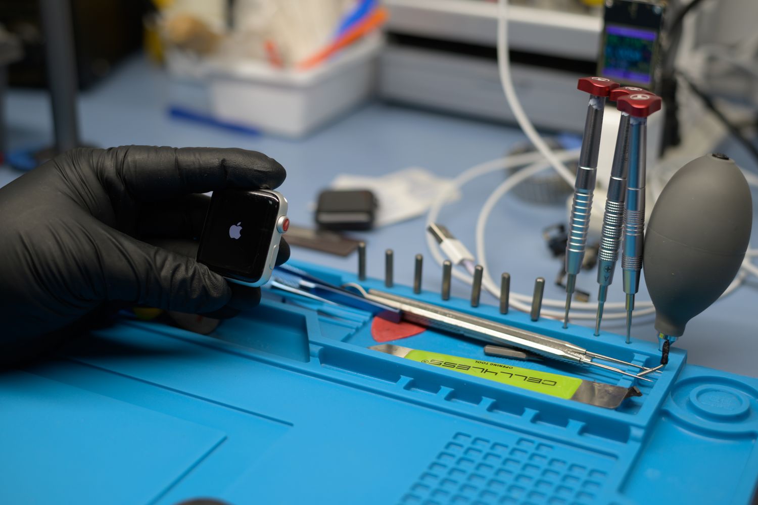 Técnico com luvas a reparar um smartwatch com ferramentas de precisão